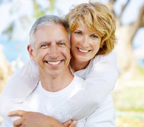 Smiling couple with dental implants in Lakeway standing outside on a bright day
