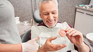 Man in maroon shirt holding new dentures and smiling