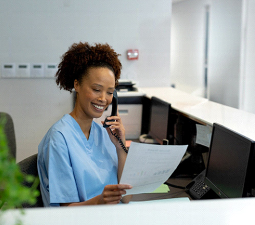 a front desk staff at a dental office looking at a piece of paper and talking on the phone
