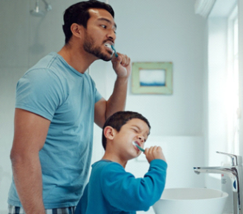 a father and son brushing their teeth together in a bathroom