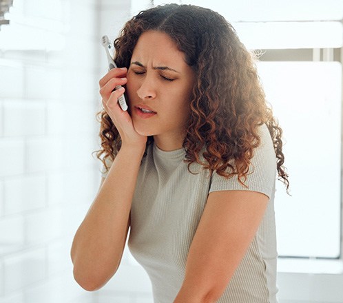Concerned woman holding her toothbrush, touching the side of her face