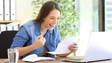 Woman cheering at her desk because dental implants are affordable