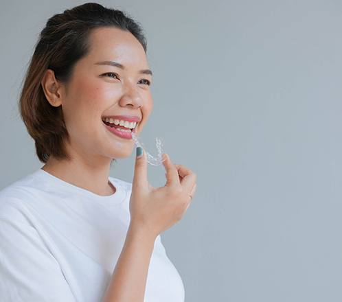 a woman smiling and holding her Sure Smile aligners