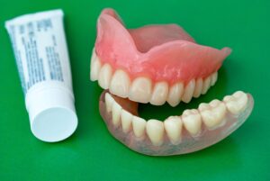 Tube of denture adhesive next to dentures on green background
