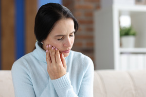 Woman in blue sweater rubbing her jaw in pain